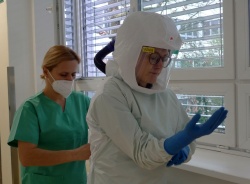 Pri oblačenju zaščitne opreme specializantki interne medicine Katarini  Čurk Dragovan pomaga diplomirana medicinska sestra Urška Kaplan.